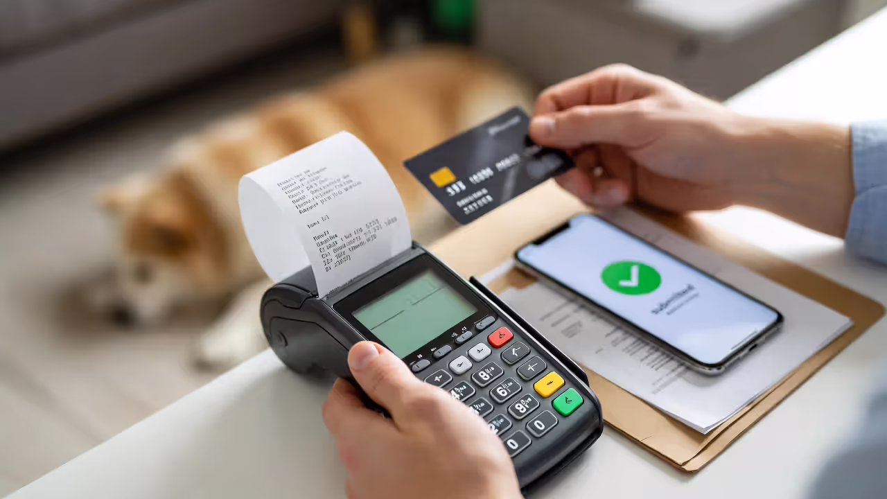 Owner paying a vet bill with a card while a phone shows a blurred claim processing status